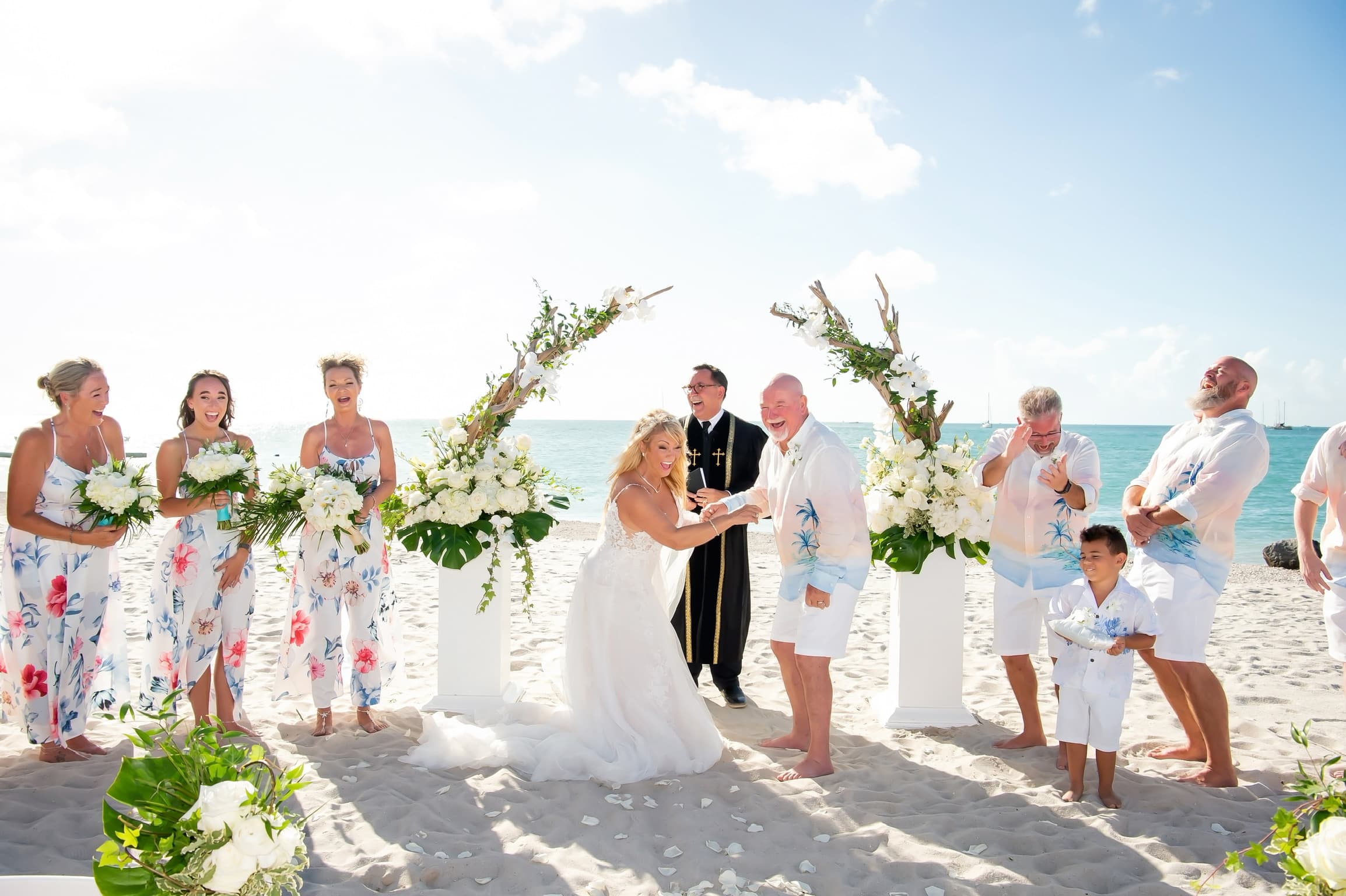 Bride and bridal party laughing together at a beachfront wedding ceremony